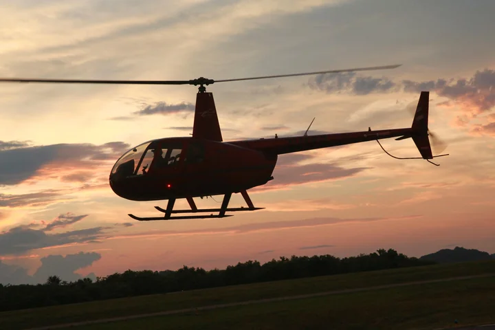 A small helicopter silhouetted against an orange evening sky