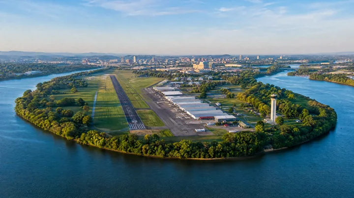 Aerial view of a small airport in a river bend with a city skyline on the horizon